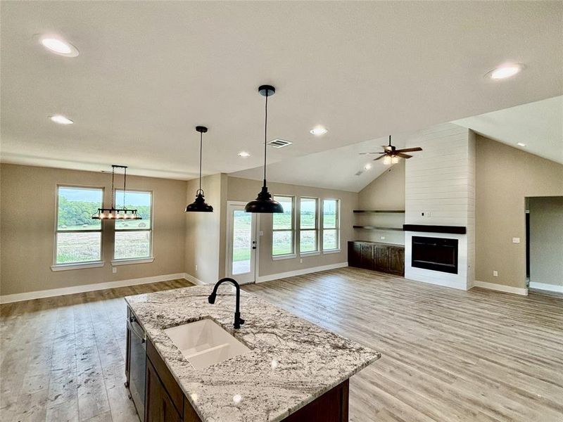 Kitchen featuring light wood-style floors, open floor plan, dishwasher, a large fireplace, and a ceiling fan Kitchen featuring light wood-style floors, open floor plan, dishwasher, a large fireplace, and a ceiling fan