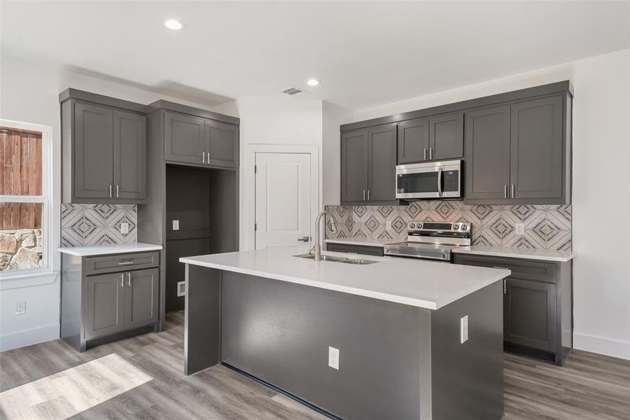 Kitchen with tasteful backsplash, appliances with stainless steel finishes, light stone countertops, light wood-style flooring, and recessed lighting