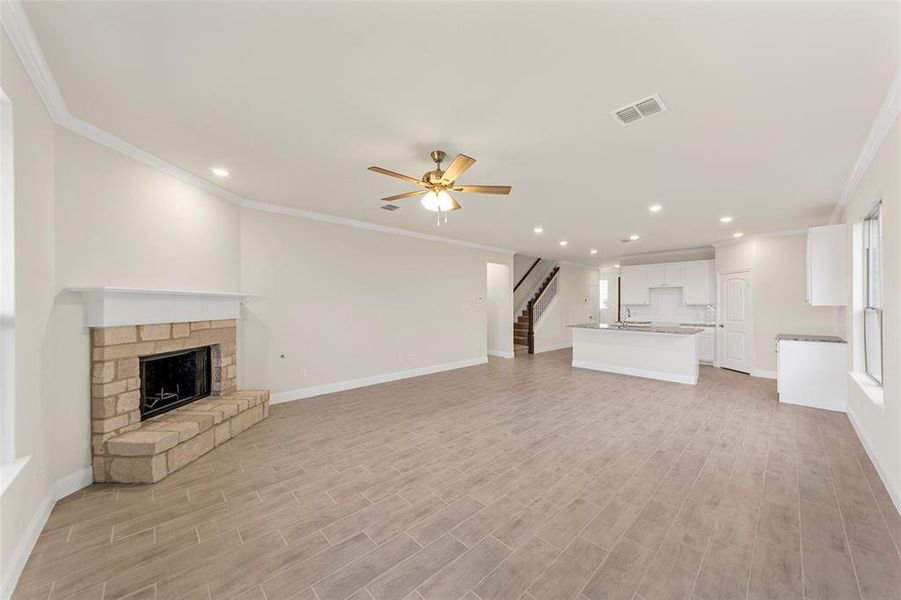 Unfurnished living room with light hardwood / wood-style flooring, a stone fireplace, ceiling fan, and crown molding