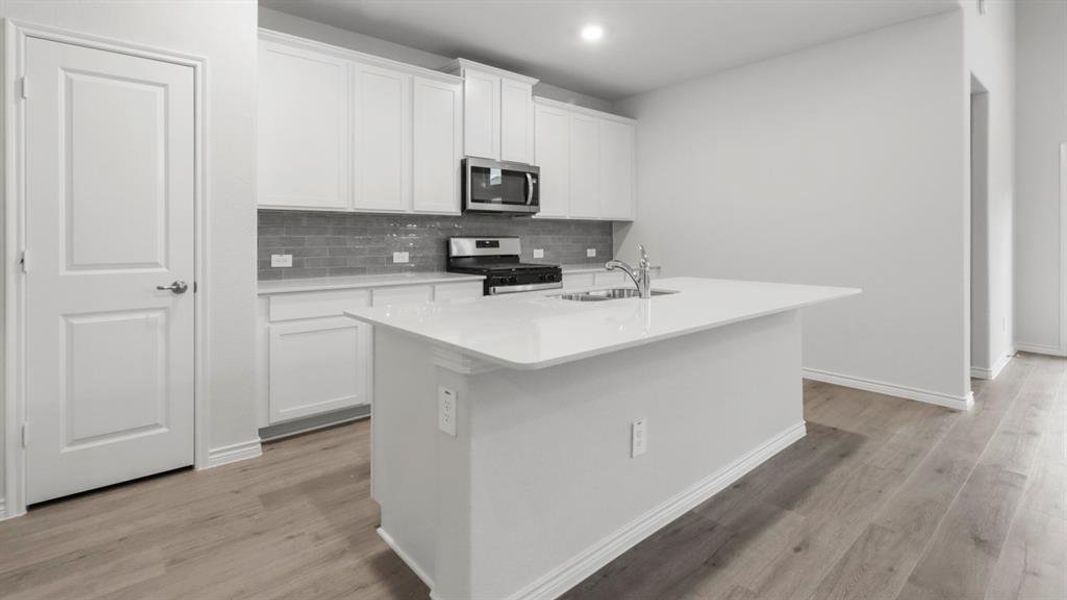 Kitchen with white cabinets, decorative backsplash, appliances with stainless steel finishes, a center island with sink, and light stone counters Kitchen with white cabinets, decorative backsplash, appliances with stainless steel finishes, a center island with sink, and light stone counters