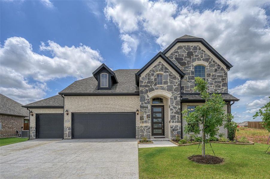French country inspired facade featuring stone siding, concrete driveway, brick siding, an attached garage, and roof with shingles
