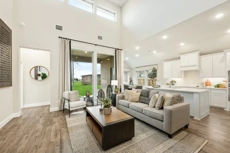 Open-concept living room with two-story ceilings, hardwood floors, and kitchen visible in background