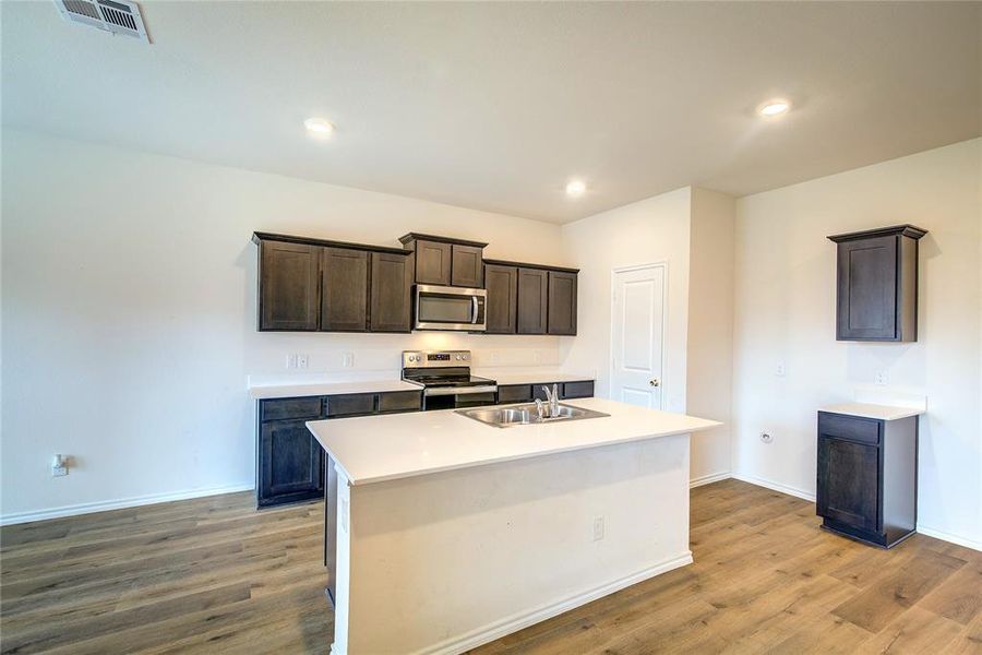 Kitchen with dark brown cabinetry, appliances with stainless steel finishes, a center island with sink, light wood-type flooring, and recessed lighting