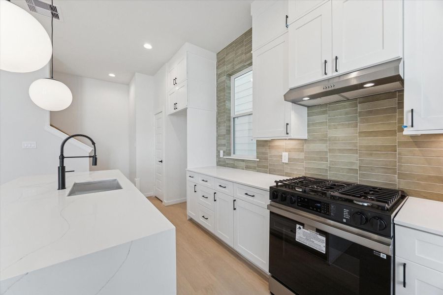 An up-close shot highlights the kitchen’s sage green backsplash, quartz countertops, and floor-to-ceiling cabinets with under-cabinet lighting and soft-close drawers and doors, showcasing the thoughtful design and modern, functional finishes.