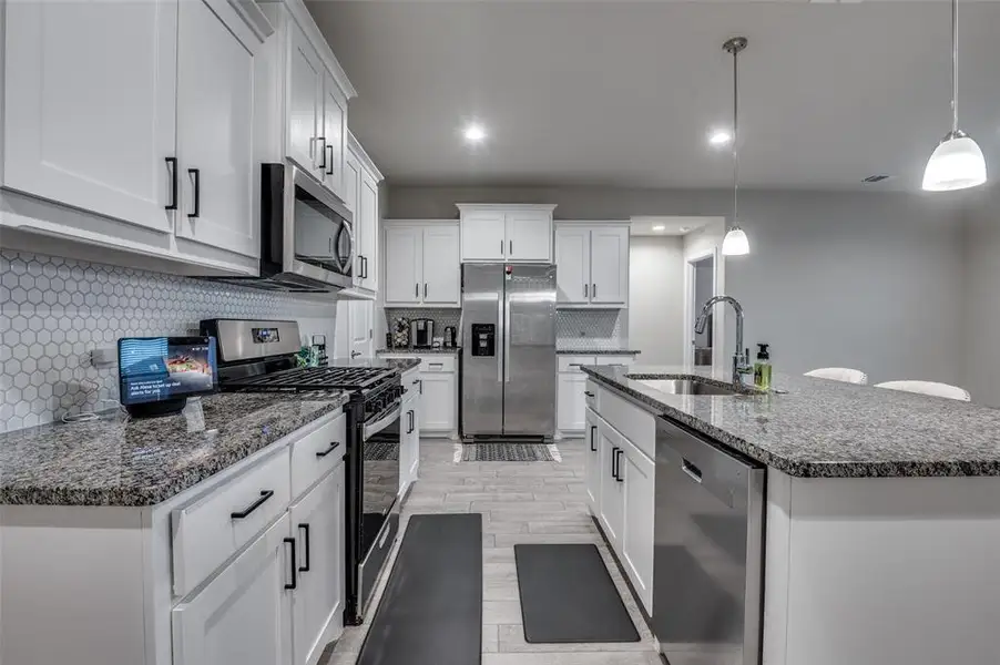 Kitchen with stainless steel appliances, dark stone countertops, white cabinetry, tasteful backsplash, and a kitchen island with sink