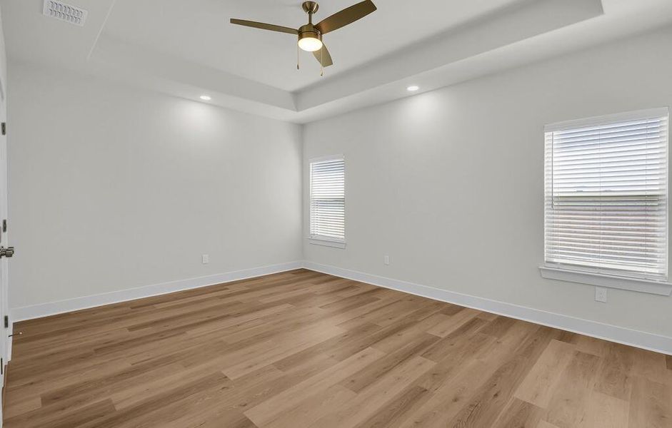 Empty room featuring a tray ceiling, light wood-style floors, a ceiling fan, and recessed lighting