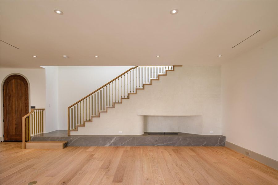 The serene living room sets the pace for everything else in the house. A sculptural plaster fireplace stretches across a raised stone platform while the open staircase above adds an architectural moment all its own, and every inch is newly finished.