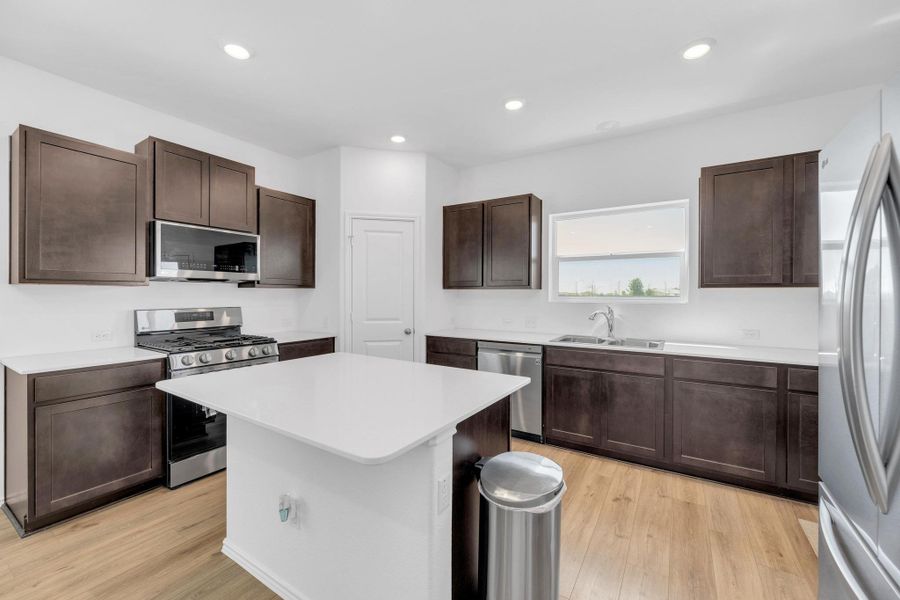 Kitchen with dark brown cabinetry, light wood-style flooring, appliances with stainless steel finishes, light countertops, and a sink