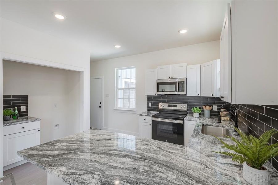 Kitchen featuring white cabinets, backsplash, light stone countertops, stainless steel appliances, and sink