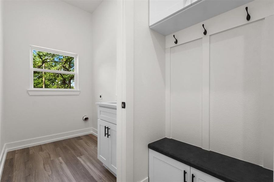 Utility area featuring wood-look flooring, a window providing natural light, a white cabinet with black hardware, and an integrated bench with storage and coat hooks