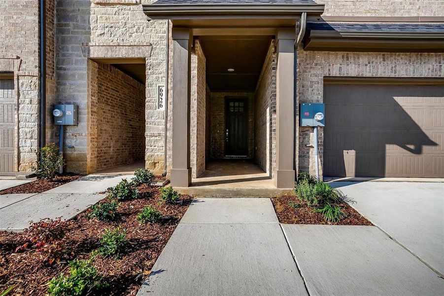 View of exterior entry featuring a garage, a shingled roof, concrete driveway, and brick siding