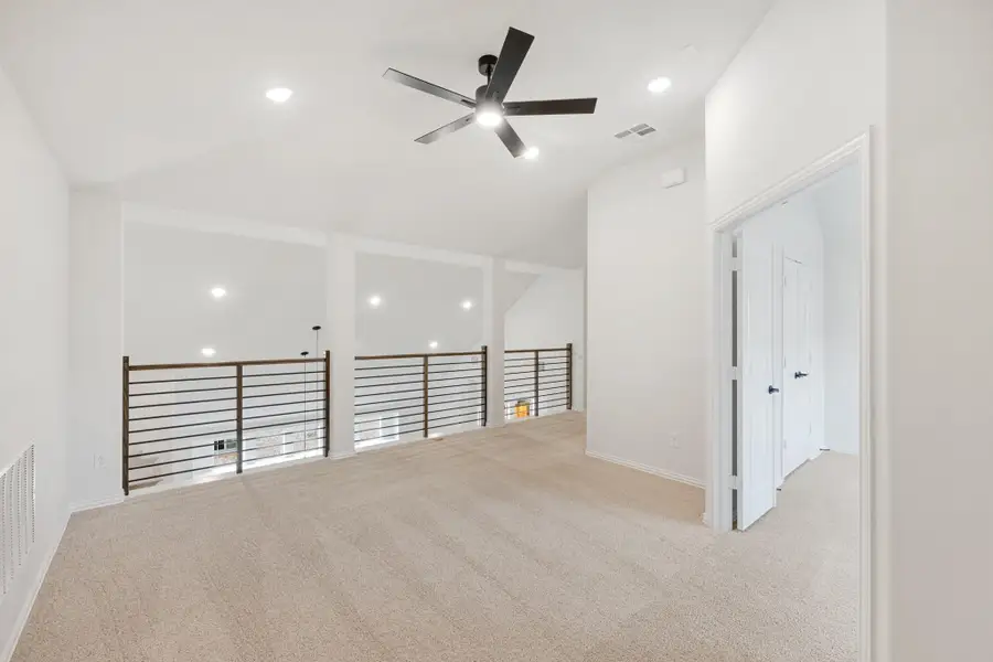Open upstairs loft with carpet, ceiling fan, and metal railing overlooking lower level