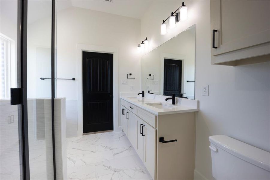 Full bathroom with double vanity, light marble finish floors, and lofted ceiling