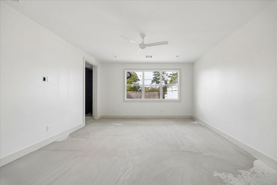 Spacious primary suite designed with simplicity and comfort in mind, featuring generous proportions, high ceilings, and a clean, modern aesthetic. A large window brings in natural light while offering views of the surrounding greenery, creating a bright and relaxing retreat. The open layout provides flexibility for a variety of furniture arrangements, with direct access to the ensuite bath for added convenience and privacy.