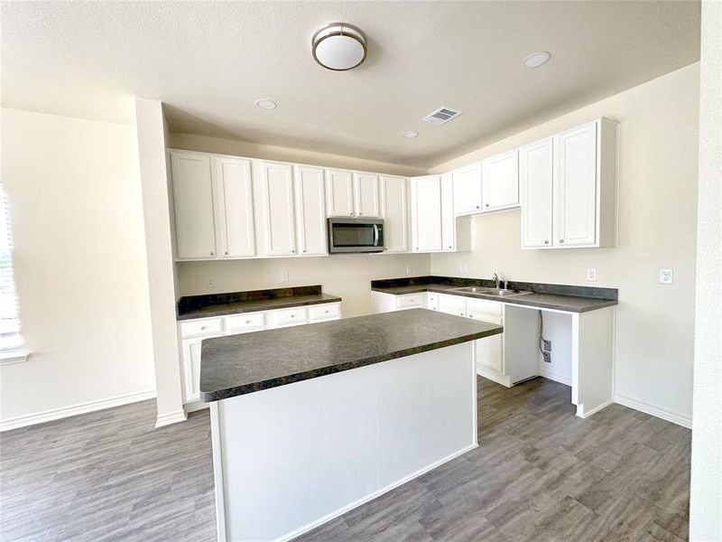 Kitchen with a kitchen island, stainless steel microwave, dark countertops, white cabinetry, and recessed lighting