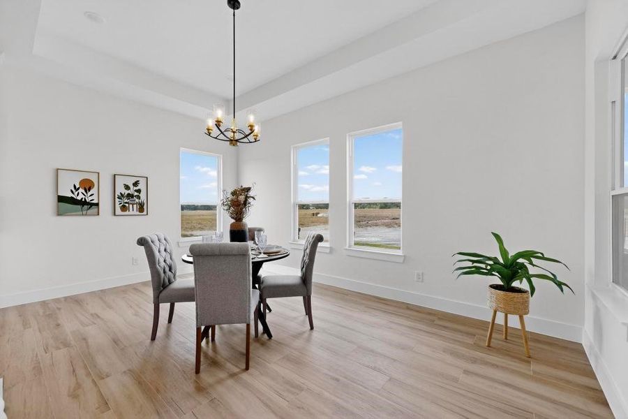 Dining area featuring a raised ceiling, light wood-style floors, and a chandelier Dining area featuring a raised ceiling, light wood-style floors, and a chandelier