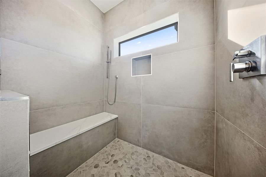 A walk-in shower features large-format wall tiles, a built-in stone bench, and a hexagonal mosaic floor.