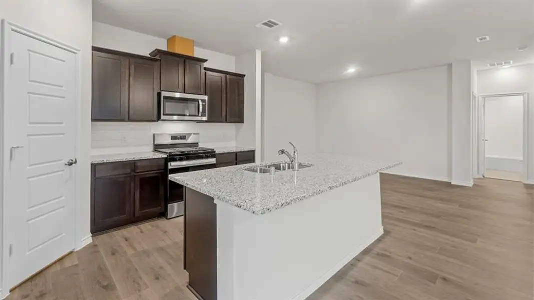 Kitchen featuring dark wood cabinetry, stainless steel appliances, a tile backsplash, light-toned granite-finish countertops, and wood-finish flooring