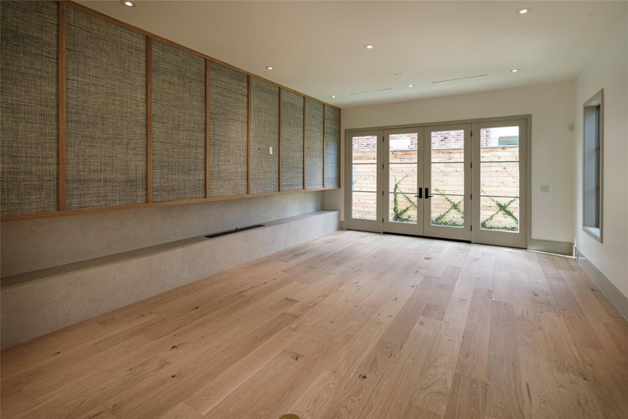 A family room with a point of view. A full wall of textured panels framed in warm wood conceals a linear fireplace within the long, streamlined hearth, while French doors open the room directly outside. Quiet, architectural, and anything but ordinary.