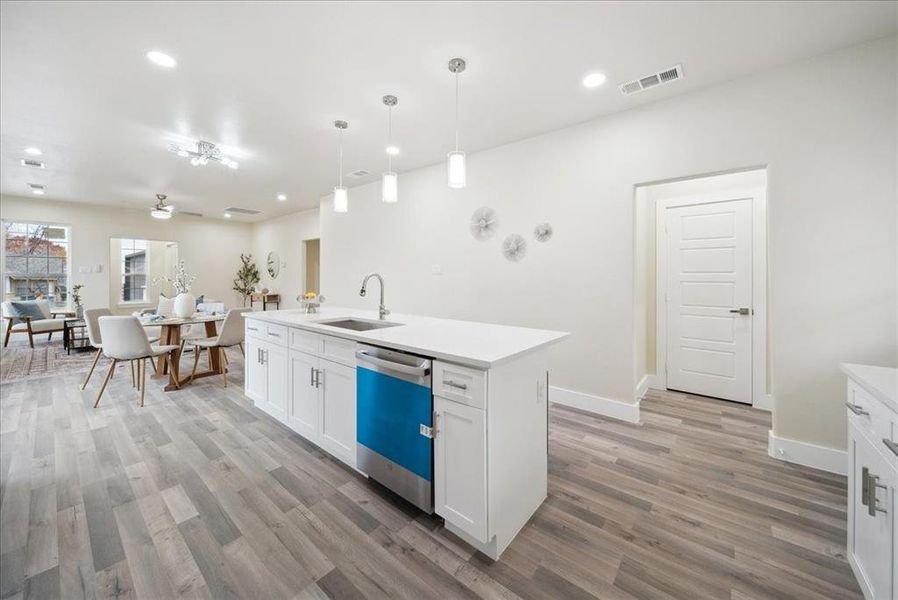 Kitchen featuring stainless steel dishwasher, sink, decorative light fixtures, a center island with sink, and white cabinetry