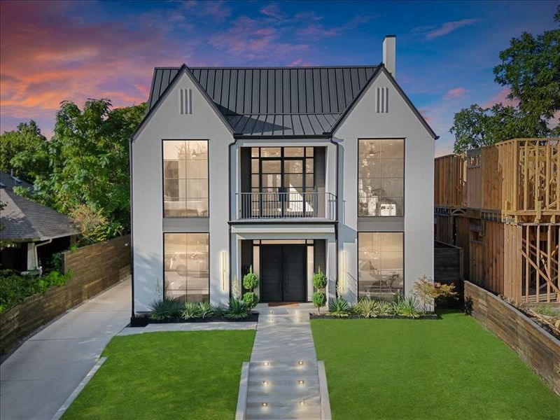 View of front of property featuring a balcony, a metal roof, a standing seam roof, a chimney, and stucco siding