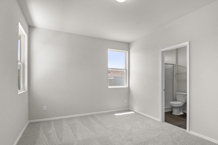 A bedroom with cream colored walls, white framed windows, and tan carpeting.