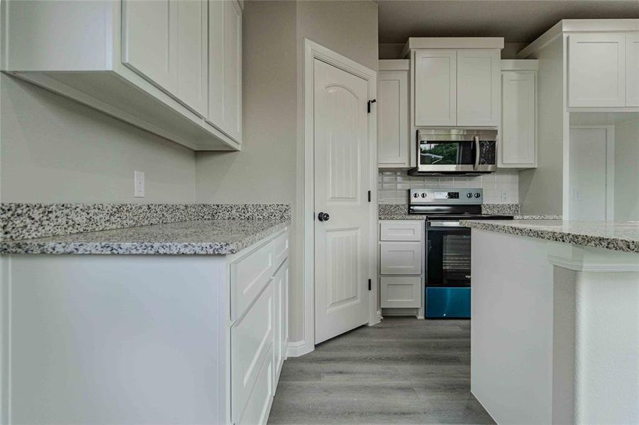 Kitchen with white cabinetry, decorative backsplash, electric range, light stone countertops, and light hardwood / wood-style floors