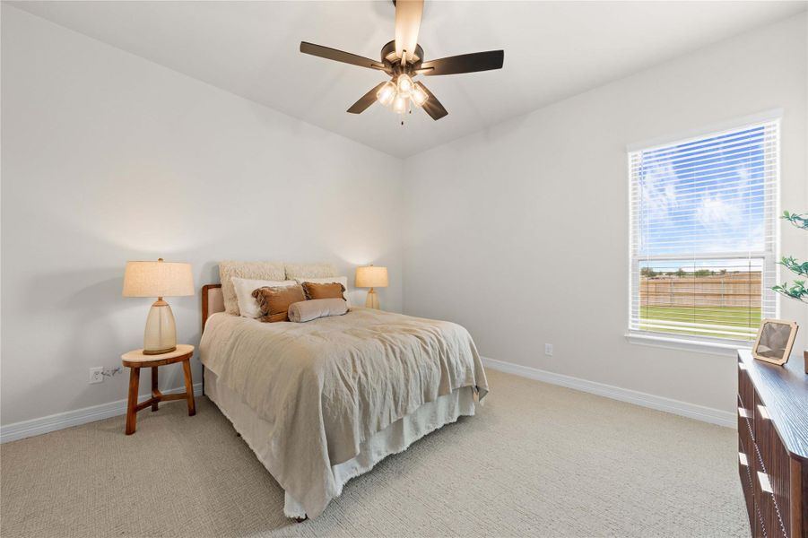 Well-lit bedroom with a ceiling fan, featuring comfortable carpeting and a large window inviting natural light. Well-lit bedroom with a ceiling fan, featuring comfortable carpeting and a large window inviting natural light.