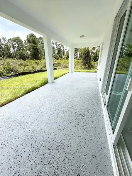 Covered concrete patio featuring a speckled finish, support columns, and sliding glass door access