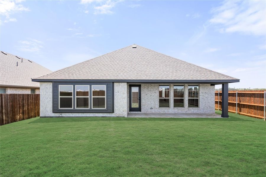 Rear exterior of single-story brick home with covered patio, large windows, and fenced backyard with green lawn.