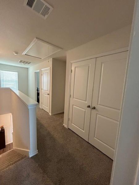 Upper level hallway featuring plush carpet flooring, white paneled doors, and a staircase with a substantial newel post