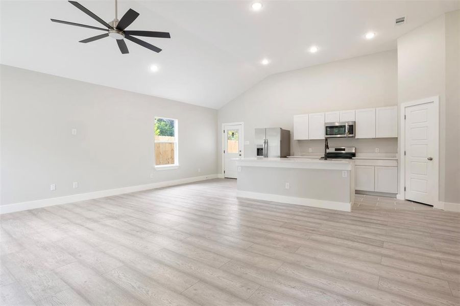 Kitchen featuring ceiling fan, light hardwood / wood-style floors, stainless steel appliances, a center island with sink, and white cabinetry