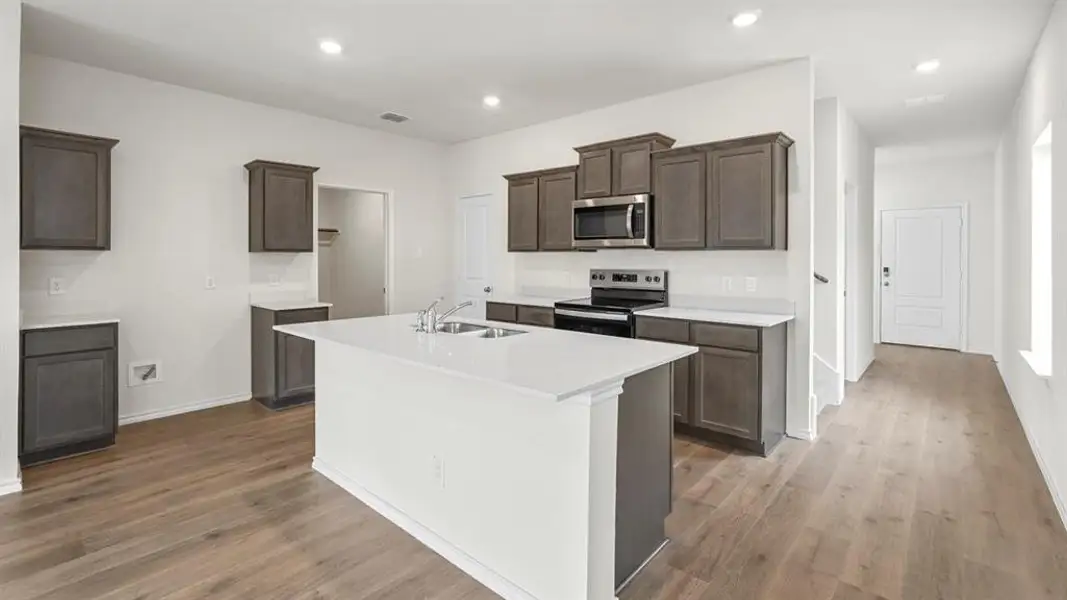 Contemporary kitchen featuring an expansive center island, integrated stainless steel appliances, wood-finish flooring, white countertops, and recessed lighting