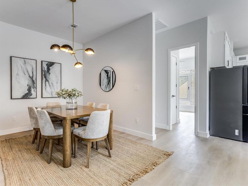Dining area featuring a contemporary gold-tone chandelier, light wood-finish flooring, and crisp white walls Dining area featuring a contemporary gold-tone chandelier, light wood-finish flooring, and crisp white walls