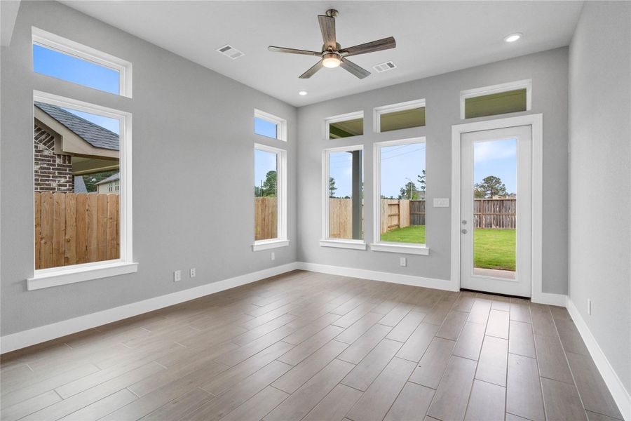 A bright and airy open-concept space featuring tile flooring, high ceilings with recessed lighting and ceiling fan, abundant natural light from large windows, and an access door to the back covered patio.