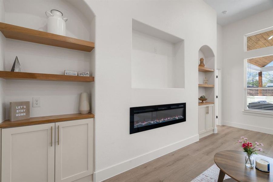 Living room featuring built in features, a glass covered fireplace, and light wood finished floors Living room featuring built in features, a glass covered fireplace, and light wood finished floors