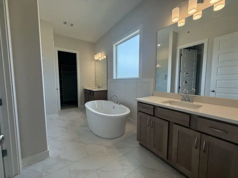 Bathroom featuring two vanities, light marble finish floors, a walk in closet, and a freestanding tub