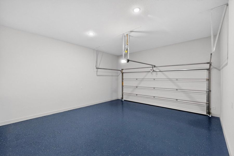 Spacious garage featuring a finished blue speckled floor, crisp white walls, and a white paneled garage door Spacious garage featuring a finished blue speckled floor, crisp white walls, and a white paneled garage door