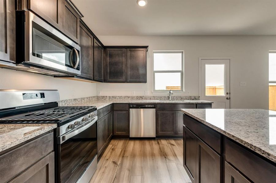 Kitchen featuring dark brown cabinetry, light stone counters, light hardwood / wood-style flooring, and stainless steel appliances