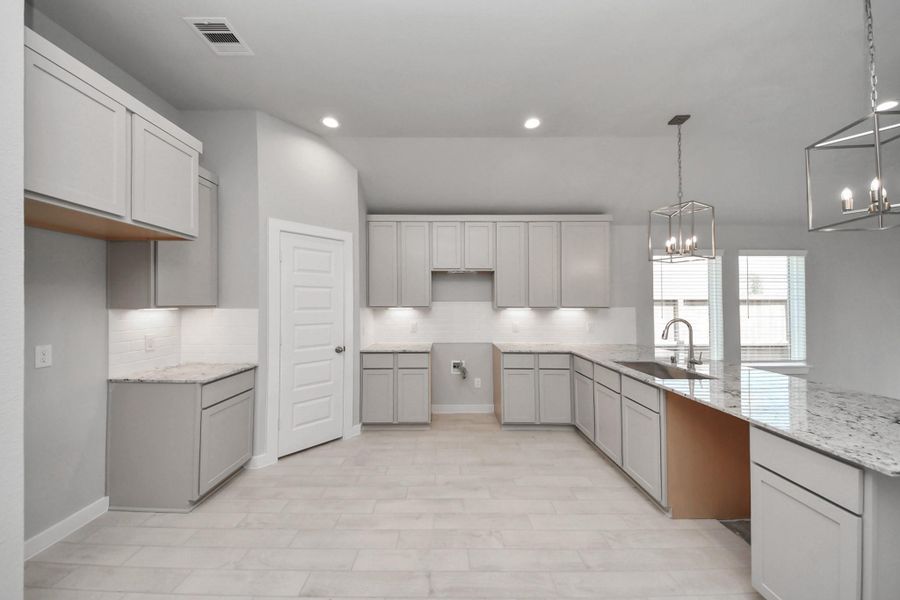 This kitchen is truly a chef's dream! This haven Boasts high ceilings, recessed & pendant lighting, stained wood cabinets, granite countertops, stainless steel appliances, a modern tile backsplash.  All of this overlooks your expansive family room, creating a perfect space for culinary delights and family gatherings. Sample photo of completed home with similar floor plan. Actual colors and selections may vary.