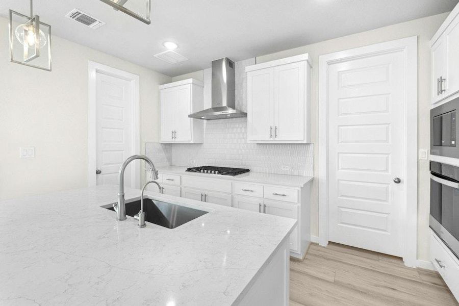 Kitchen featuring white cabinets, backsplash, wall chimney range hood, light stone countertops, and appliances with stainless steel finishes