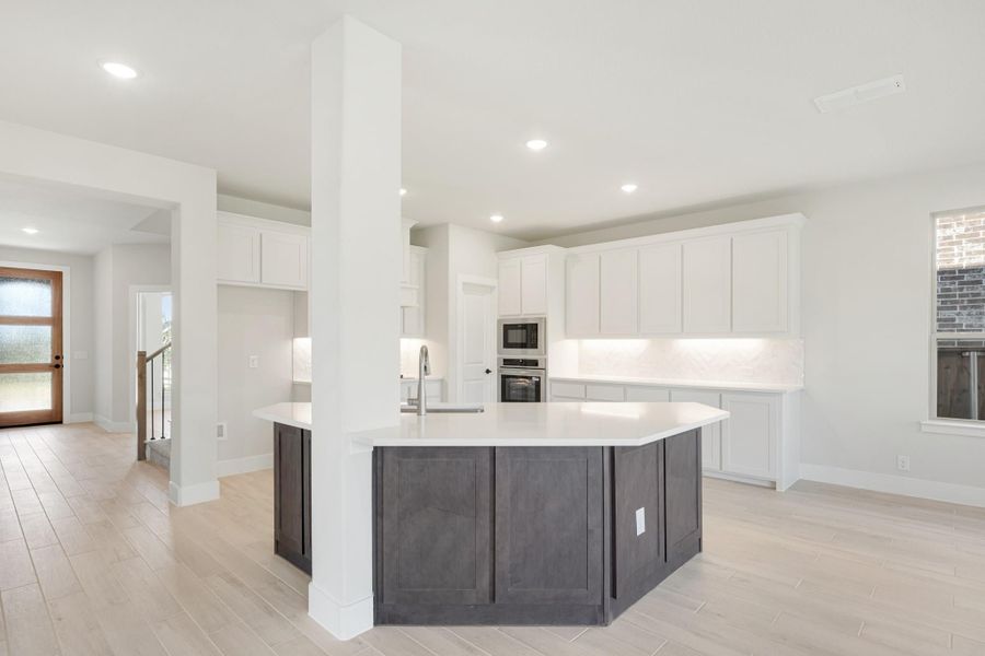Open kitchen with dark gray island, white cabinets, stainless appliances, and light wood floors