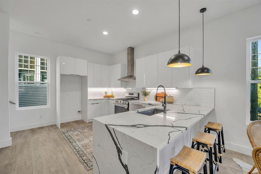 Kitchen featuring pendant lighting, stainless steel range with gas cooktop, white cabinetry, kitchen peninsula, and wall chimney exhaust hood