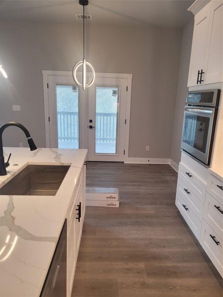 Kitchen with white cabinets, hanging light fixtures, oven, and light stone countertops