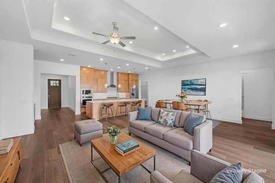 Open-concept living area featuring wood-finish flooring, a tray ceiling with recessed lighting, and a contemporary ceiling fan