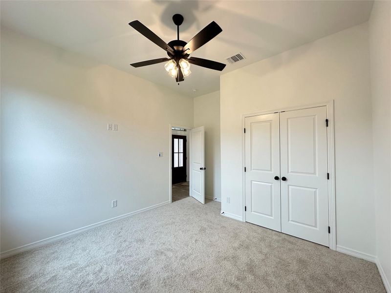 Neutral tone carpeted room featuring a ceiling fan with light kit, white bi-fold closet doors with black hardware, and crisp white walls