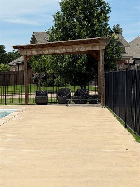 Outdoor pergola structure located inside the community pool area surrounded by a black metal perimeter fence