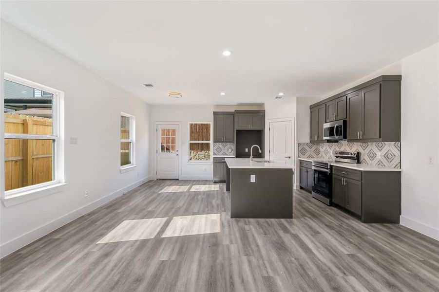 Kitchen with tasteful backsplash, stainless steel appliances, a center island with sink, light wood finished floors, and recessed lighting