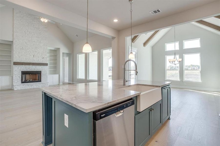 Kitchen with beam ceiling, an island with sink, stainless steel dishwasher, light hardwood / wood-style flooring, and decorative light fixtures