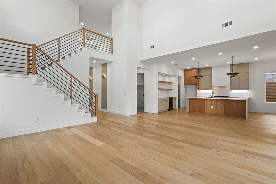 Unfurnished living room with recessed lighting, stairs, a towering ceiling, and light wood-type flooring